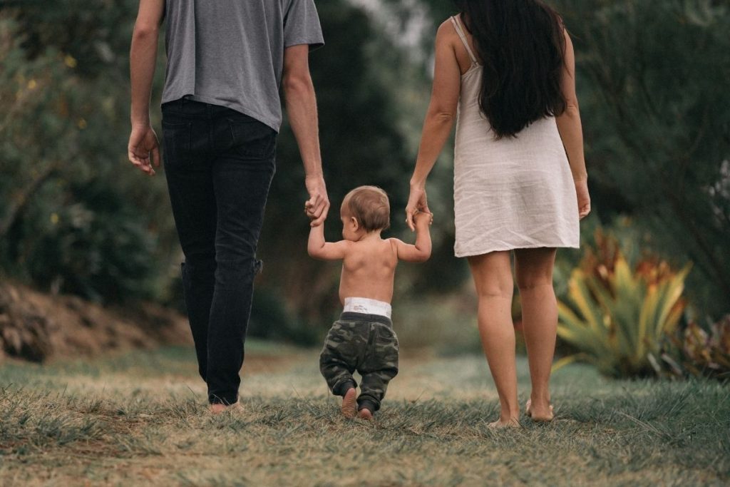 mom and dad holding hands with a toddler out for a walk