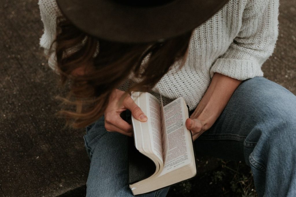 get to know the author of the bible, a woman with dark hair wearing a hat is thumbing through the Bible