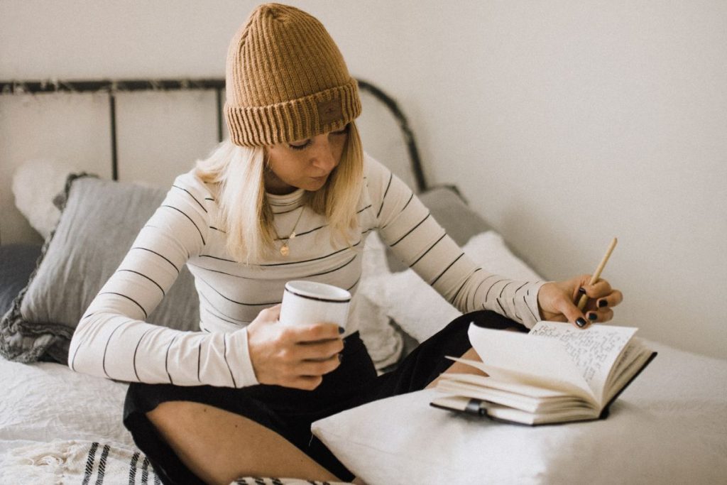 A woman sitting in bed with a cup of coffee writing in her journal