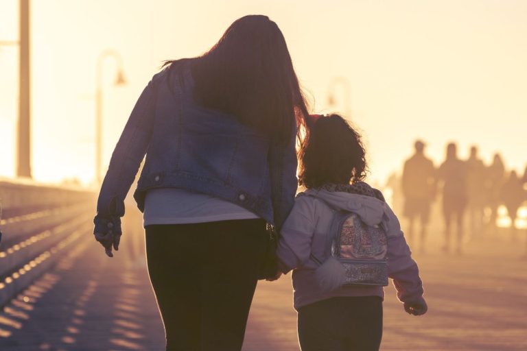 Mother and daughter walking and holding hands along a pier as the sun sets