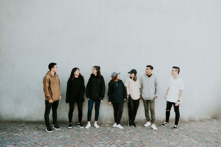 A group of men and women standing outside against a white wall