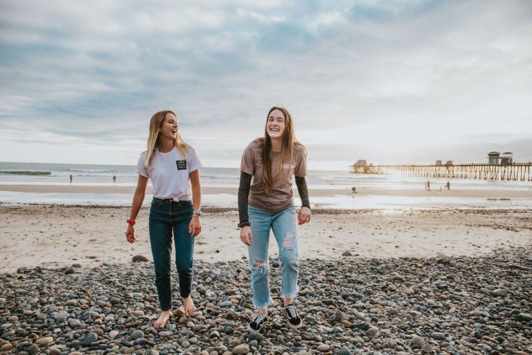 two young women walking in the sunlight on the beach in the sand away from the water