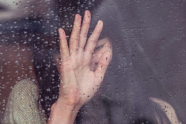 A woman with her hand on the window while it rains