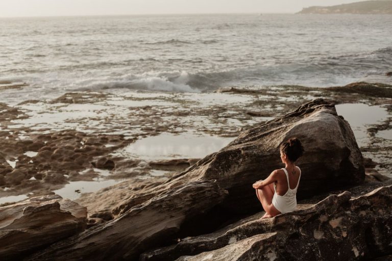 a woman sitting on the rocks looking out at the water