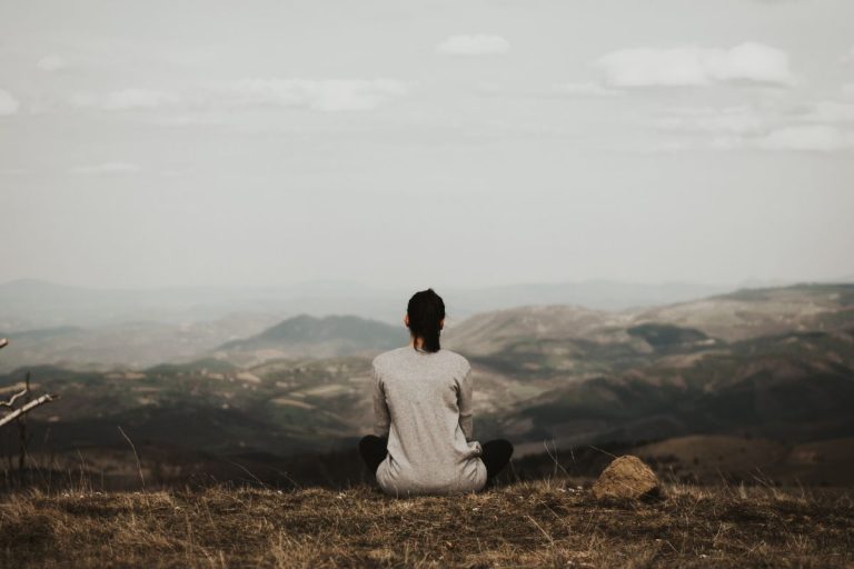 a woman sitting on a mountain side staring out into the openness