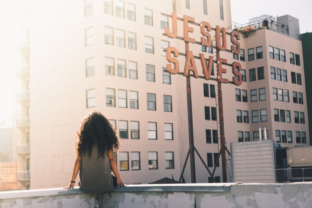 woman sitting on a roof top facing a sign that says Jesus saves