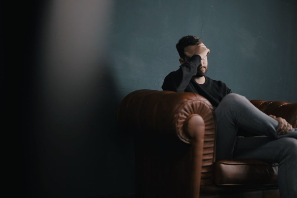a man presumably at therapy sitting on a couple with his head in his hand