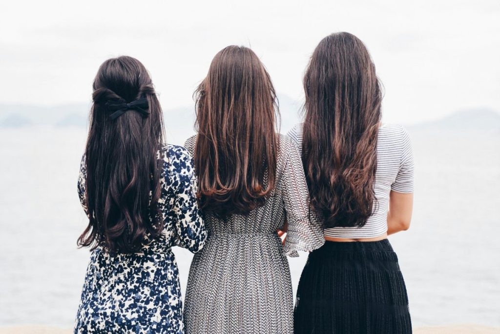 three women standing with their backs to the camera, all three have long dark hair