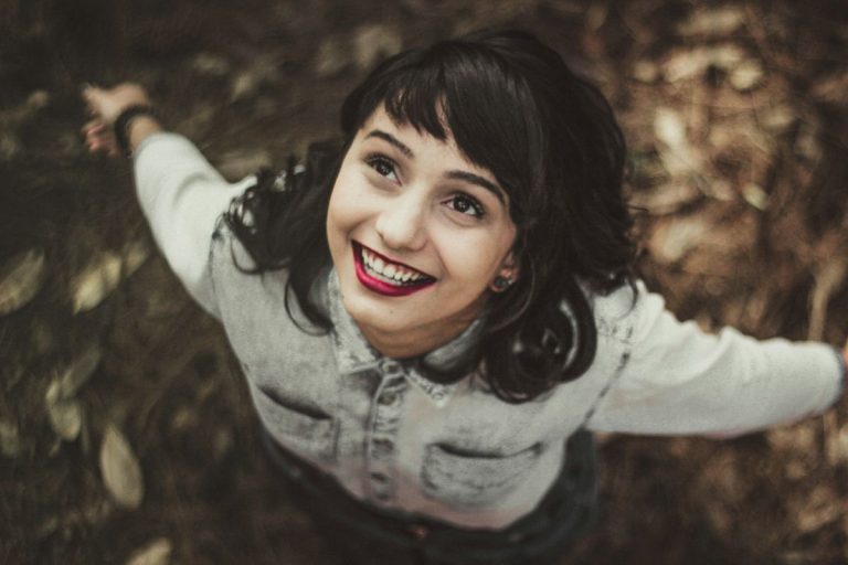a woman smiling and staring up at the sky with her arms open out wide