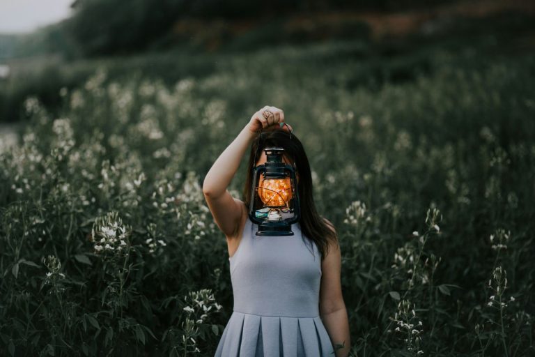 woman holding a lantern and shining a light in the middle of a field with tall grass