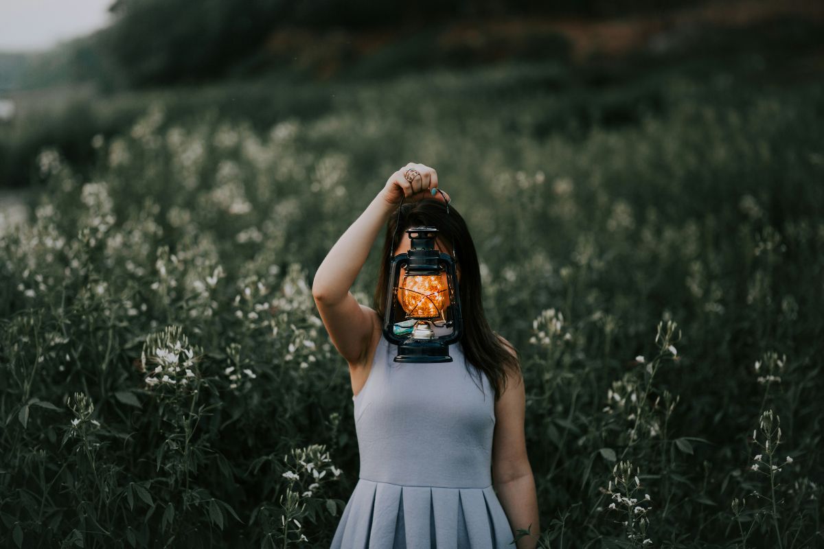 woman holding a lantern and shining a light in the middle of a field with tall grass