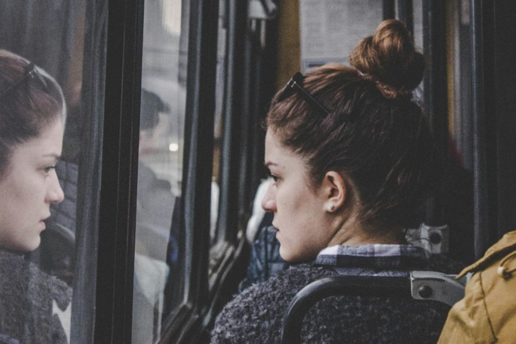young woman riding the bus and staring at her reflection in the window