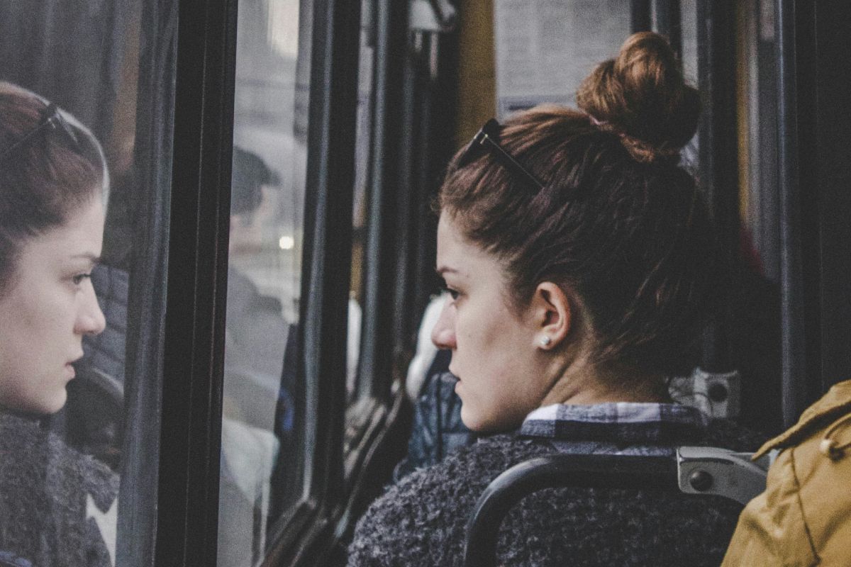young woman riding the bus and staring at her reflection in the window