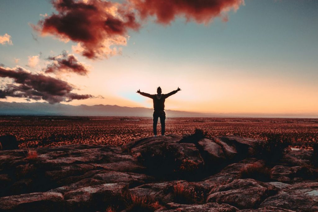 a man standing outside praising God with his hands elevated toward the sky at either sunset or sunrise