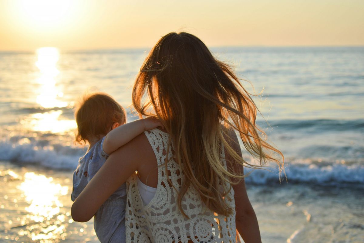 a mother holding her baby walking along the surf line on the beach at sunset