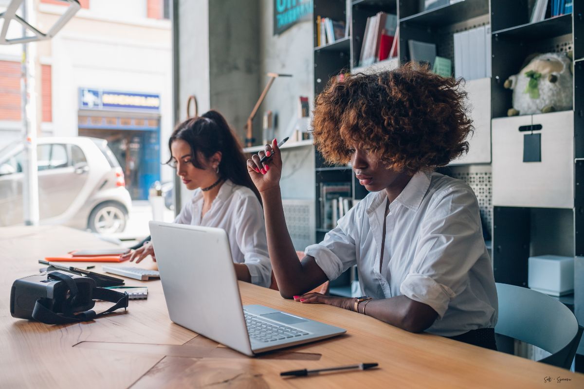 two women sitting at a table with open laptops