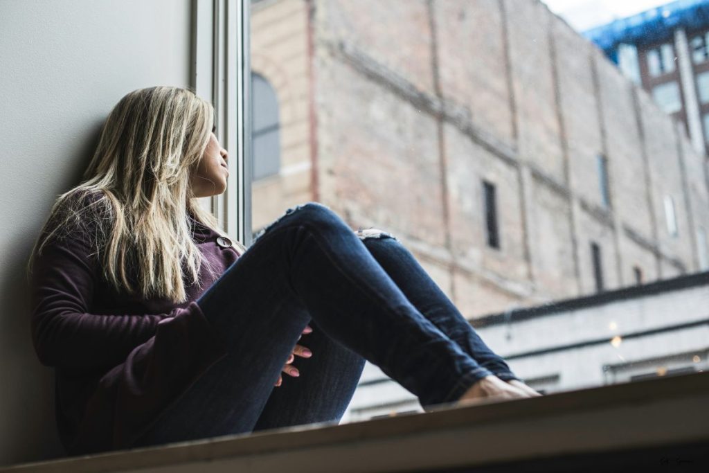 a woman sitting inside along a window ledge staring outside