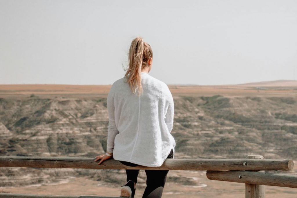 woman sitting on a fence post looking out at the hills and mountains