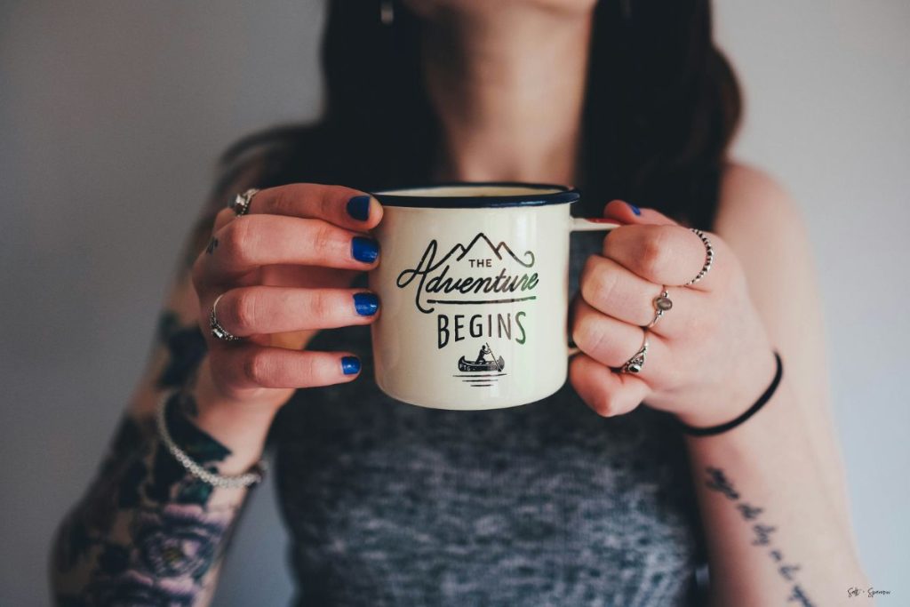 a woman holding a coffee mug that says the adventure begins