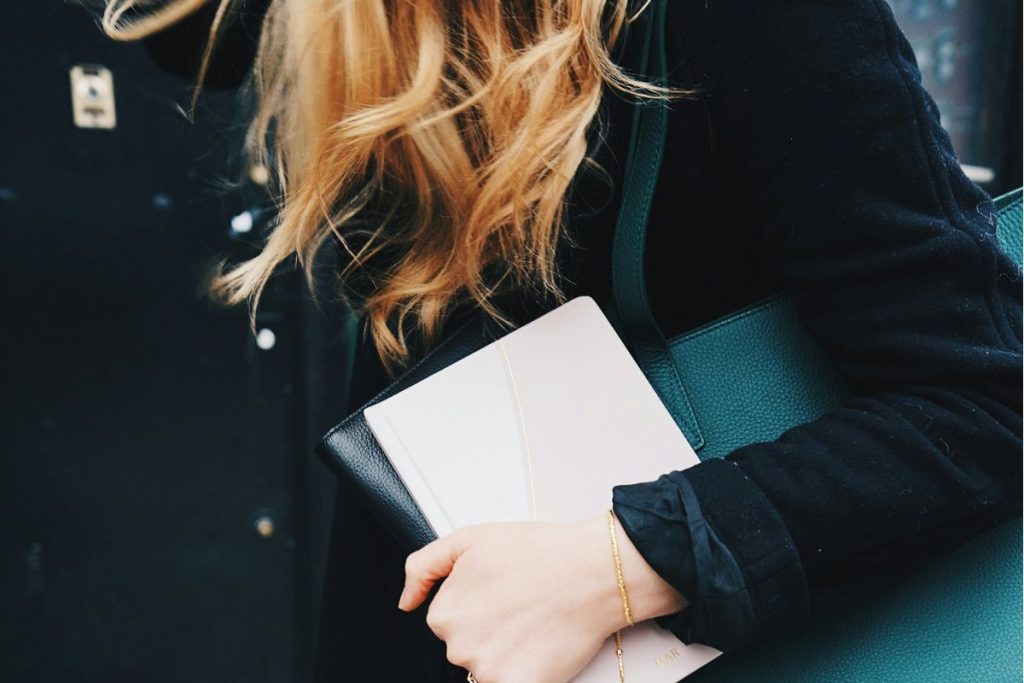 a woman walking holding her notebooks and padfolios