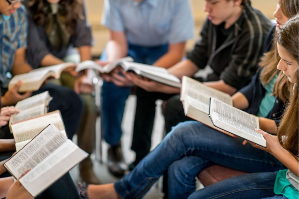 a group of young adults sitting close together in a circle in fellowship with their Bibles open