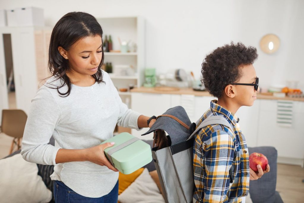 mom packing her son's lunch for school in his backpack