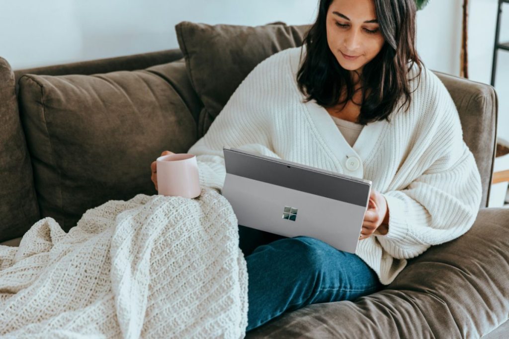 woman sitting on the couch watching something on her laptop while holding a coffee mug