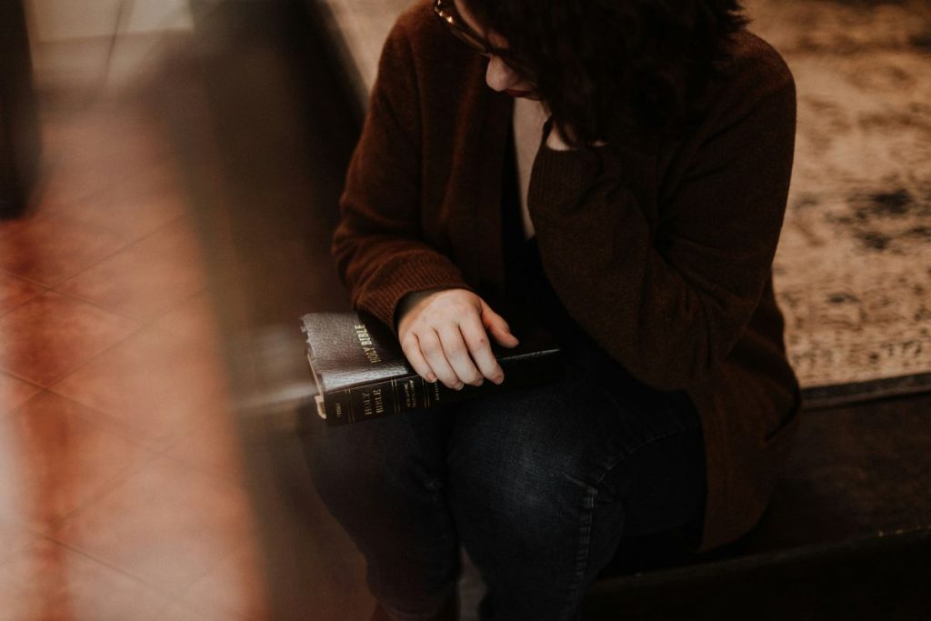 Bible verses for anxiety - a woman sitting with her head in one hand while holding a Bible on her lap with the other hand