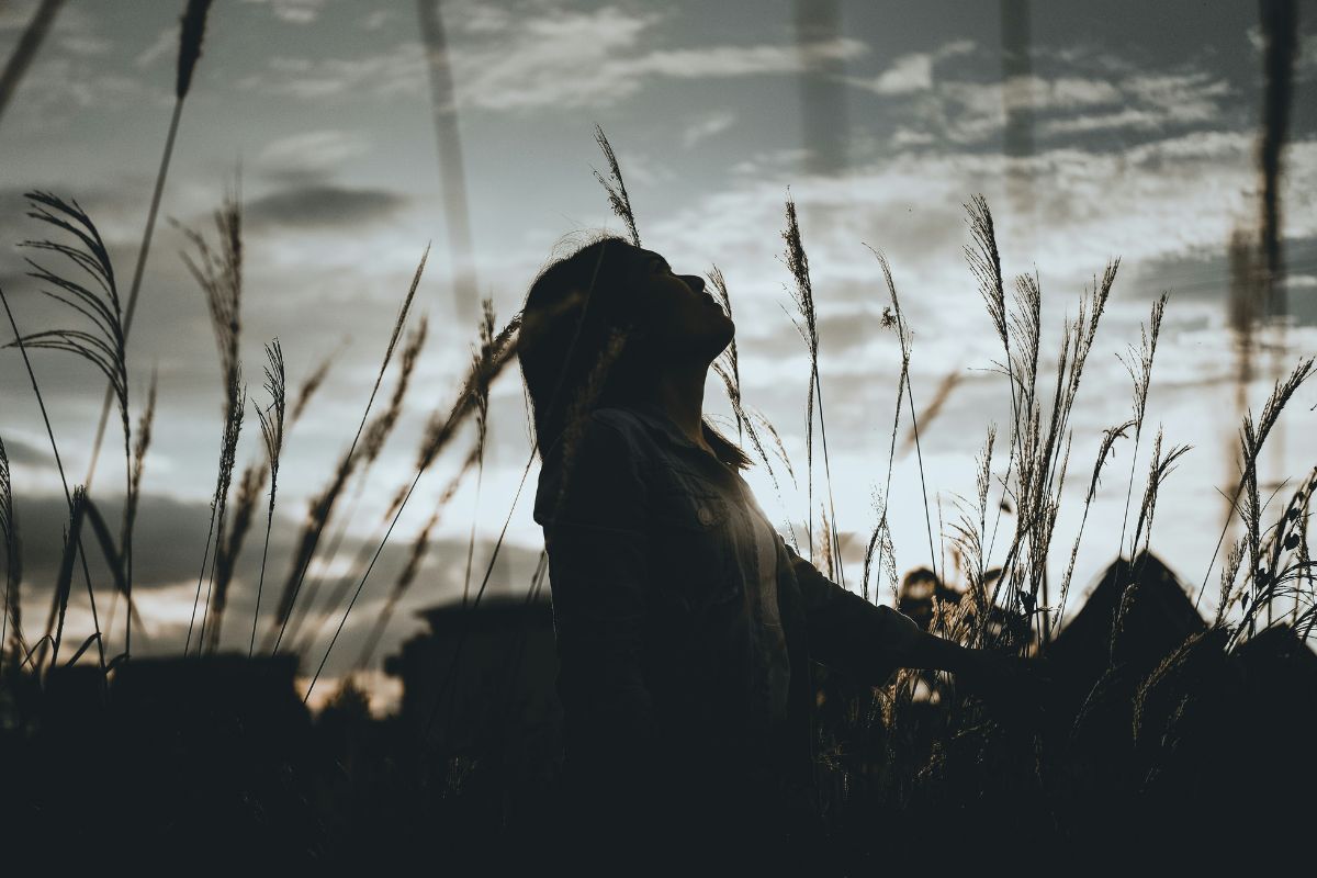 a woman in the middle of the field staring up at the sky almost as if in prayer