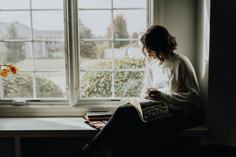 woman sitting at her window with a cup of coffee in one hand and an open bible on her lap