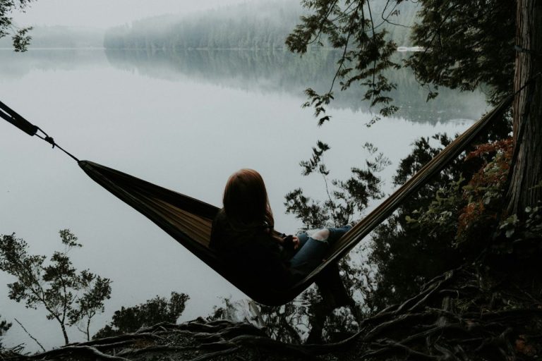 a woman sitting in a hammock staring out at a big lake enjoying the comfort of silence