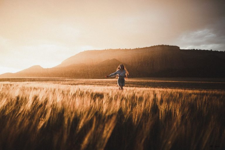 a woman running through a field at sunset