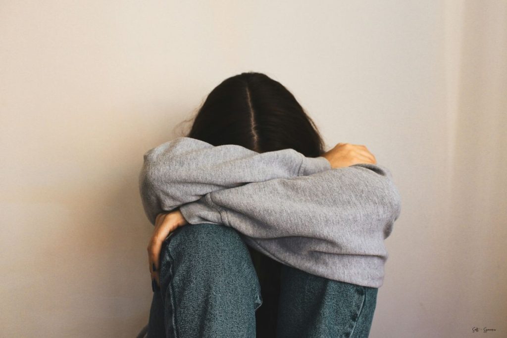 a woman sitting against a wall with her head in her arms