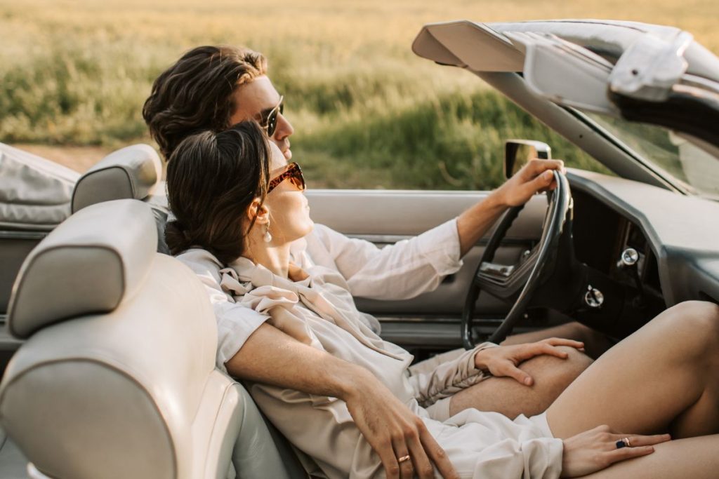 married couple in their car, the husband is driving and has one arm around his wife