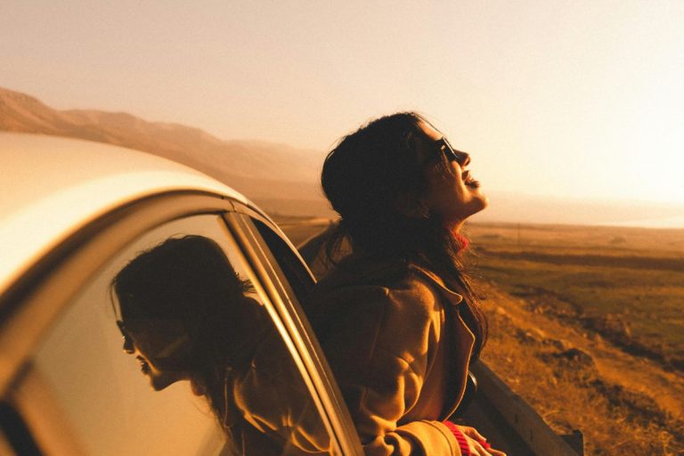 a woman leaning out a passenger car window with her face smiling toward the sky