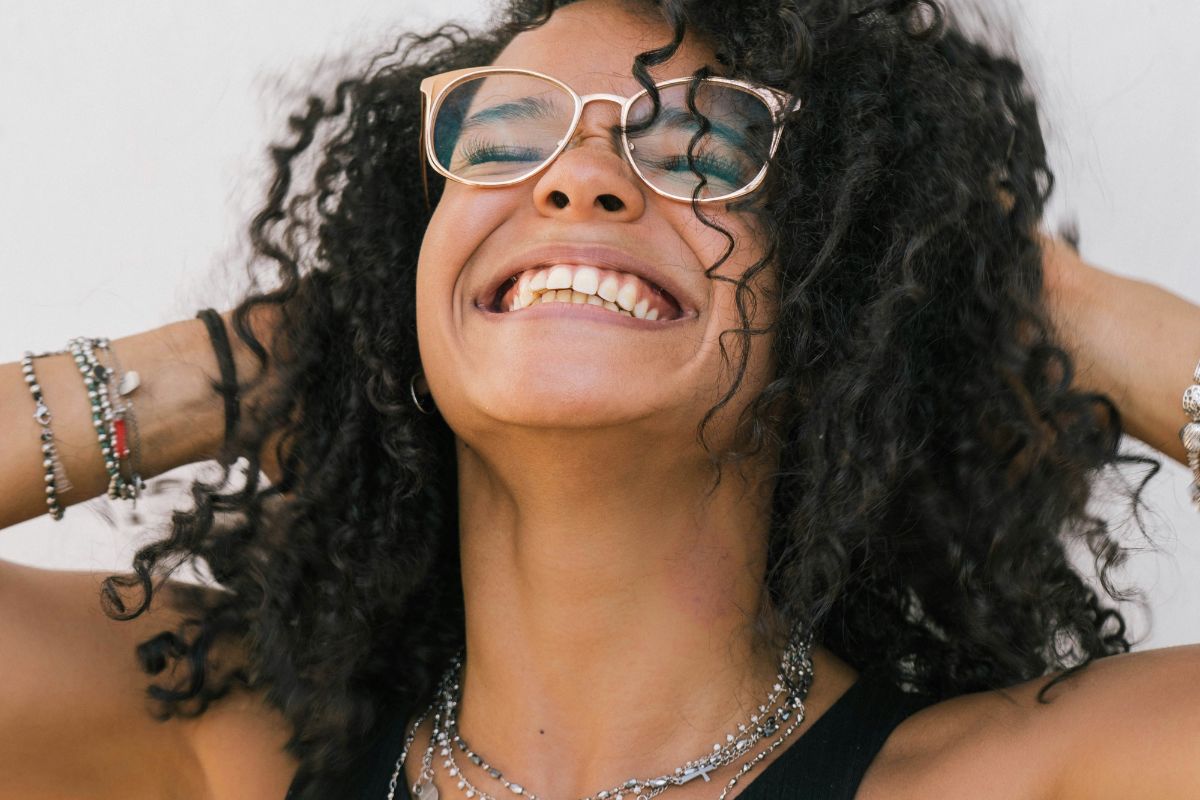 a girl in glasses smiling up at the sky with her eyes closed
