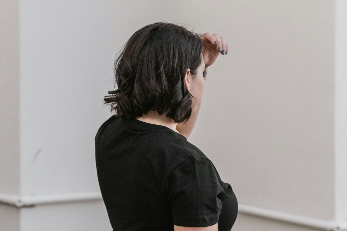 a woman with her back to the camera, hand raised to her forehead like she's looking out at the distance