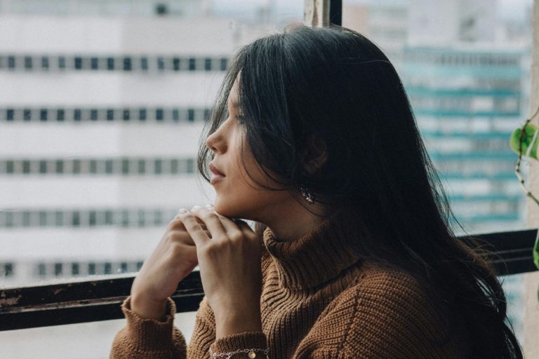 a woman with her chin resting on her hands staring out the window as if in thought