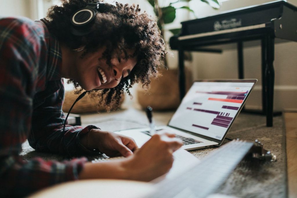 a woman listening to her headphones while working at her laptop and she's smiling